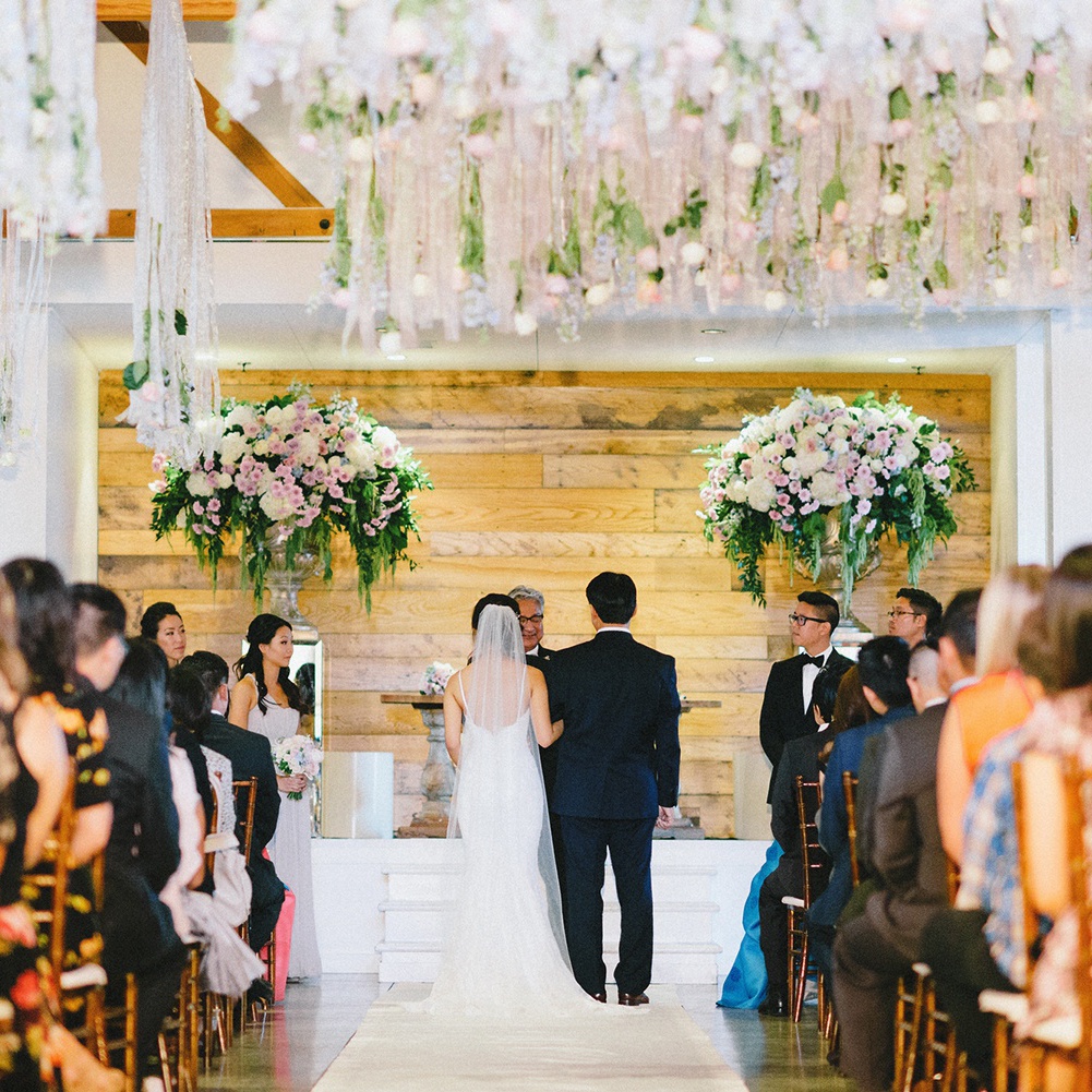 A wedding couple stand across the aisle while the audience stands for the wedding ceremony