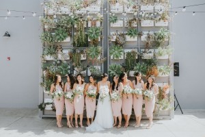 A bride and bridesmaids pose together with bouquets in front of a wall of succulent outside The Colony House