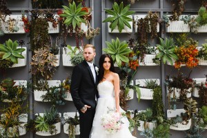 A bride and groom stair in opposite directions in front of a wall of succulents on The Colony House Patio