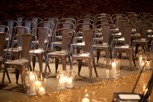 A close view of chairs and an aisle decorated with sequins and white, lit candles